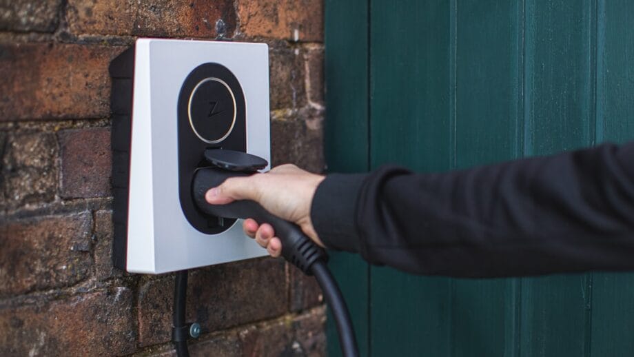 Person plugging a cable into a wall-mounted charging station against a brick wall.