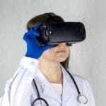 Person in a white lab coat and blue gloves wearing a virtual reality headset, with a stethoscope around their neck.