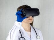 Person in a white lab coat and blue gloves wearing a virtual reality headset, with a stethoscope around their neck.