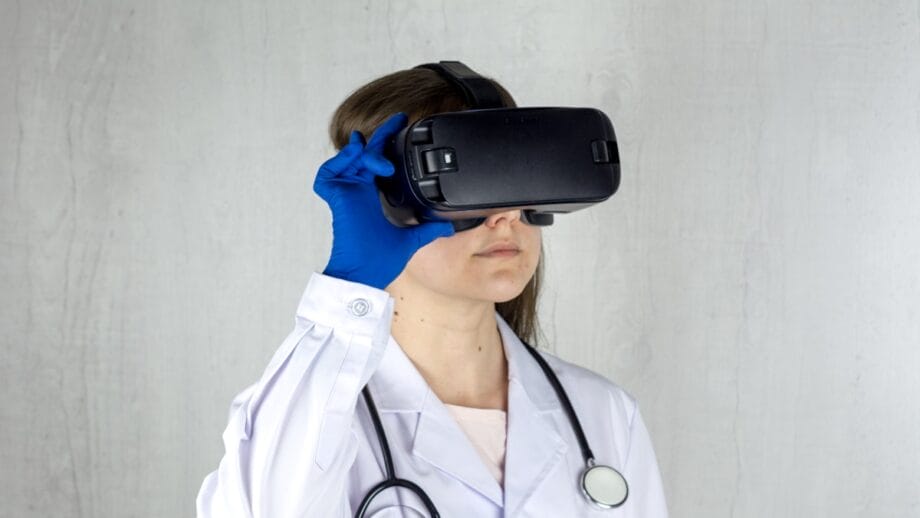 Person in a white lab coat and blue gloves wearing a virtual reality headset, with a stethoscope around their neck.