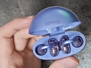 A hand holding an open blue case with two Sanag S6S Open Ear Clip Earphones inside.