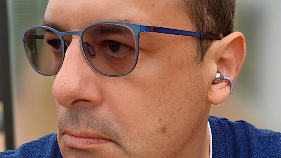 Man wearing blue-framed glasses and Sanag S6S Open Ear Clip Earphones looks to the side. Close-up shot.