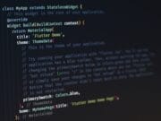 Close-up of computer screen displaying programming code for a Flutter app, featuring definition, widget build method, and theme data settings.