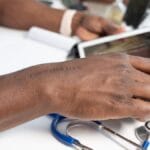 A person using a tablet at a desk with a stethoscope and pen nearby.