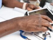 A person using a tablet at a desk with a stethoscope and pen nearby.