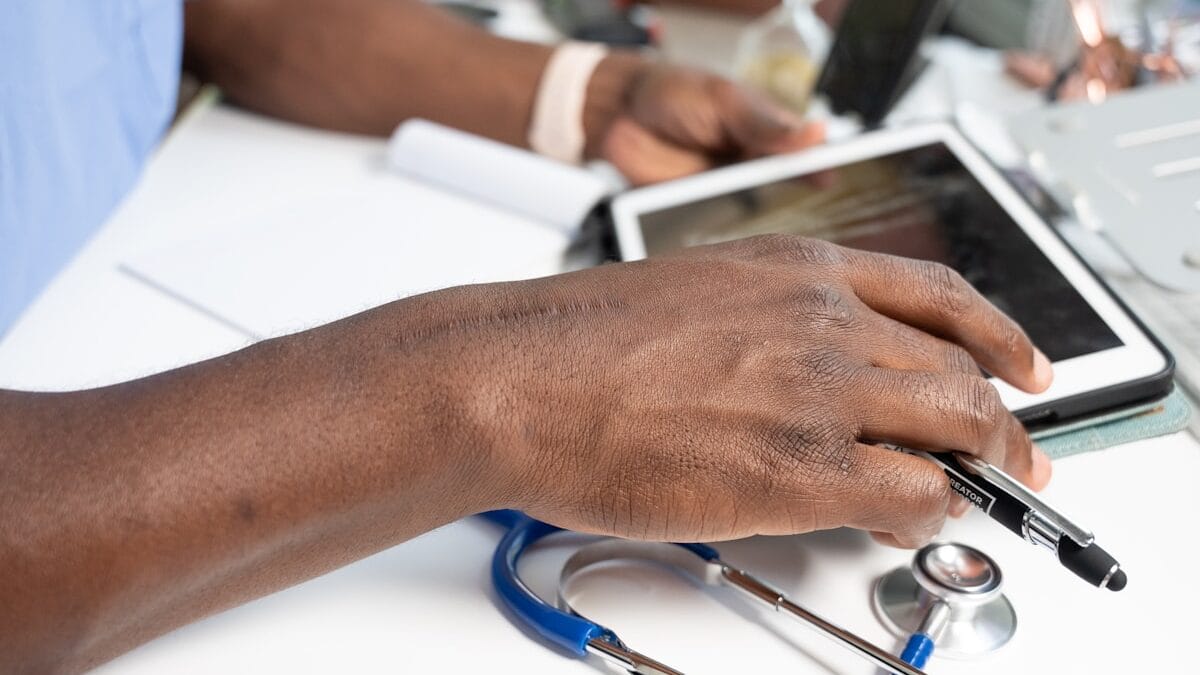 A person using a tablet at a desk with a stethoscope and pen nearby.