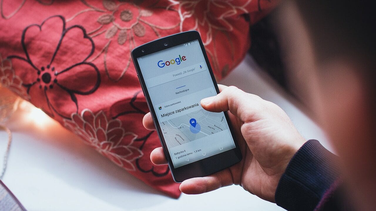 A person holding a smartphone displaying a Google Maps search with a blue location pin icon.