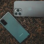 Two smartphones, one Samsung and one with a triple camera setup, lie on grass.