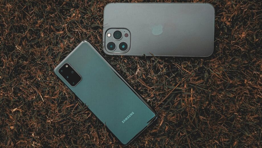 Two smartphones, one Samsung and one with a triple camera setup, lie on grass.