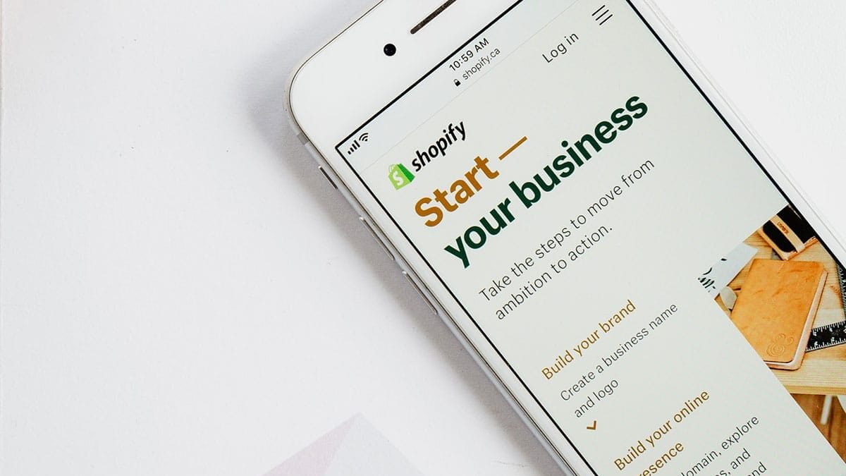 Smartphone displaying a Shopify website encouraging users to start and build a business, with navigation options visible on the screen.