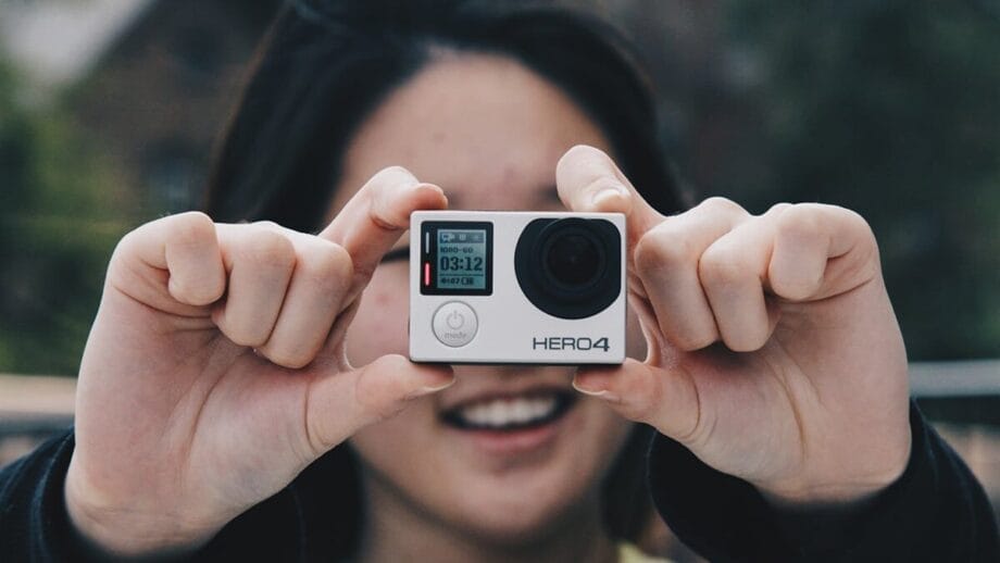 Person holding a GoPro HERO4 camera in front of their face, smiling. Background is blurred.