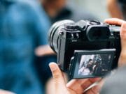 Person holding a camera, capturing an image of two people displayed on the camera's screen.