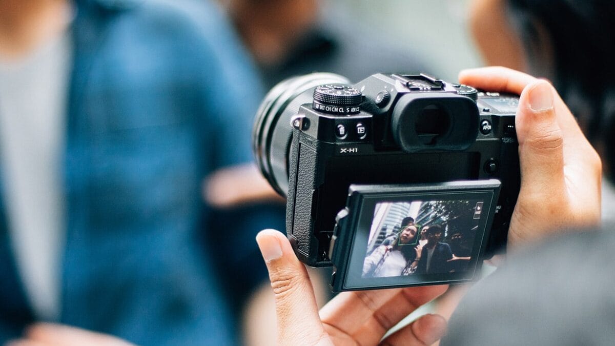 Person holding a camera, capturing an image of two people displayed on the camera's screen.