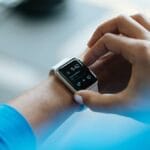 A person interacts with a smartwatch displaying the time, date, and notifications.