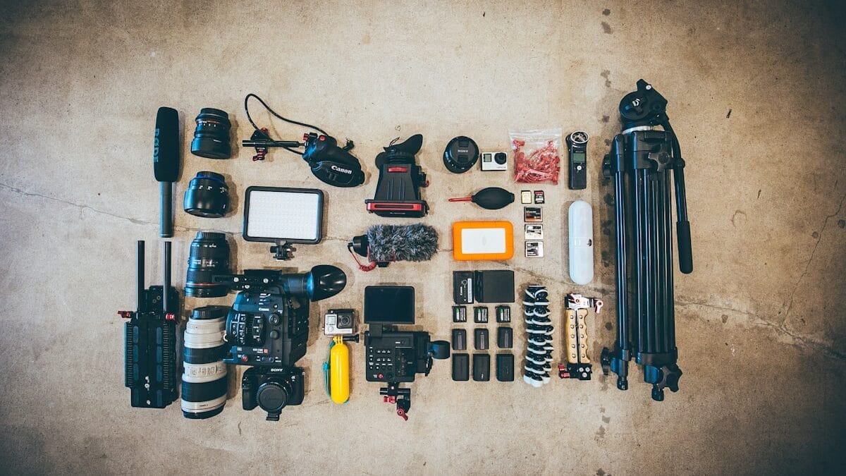 Aerial view of assorted camera equipment and accessories on a concrete floor. Items include cameras, lenses, tripods, a microphone, batteries, and more.