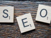 Wooden Scrabble tiles spell "SEO" on a wooden surface.