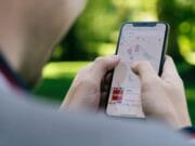 Person using a smartphone to navigate with a map app outdoors in a park setting.