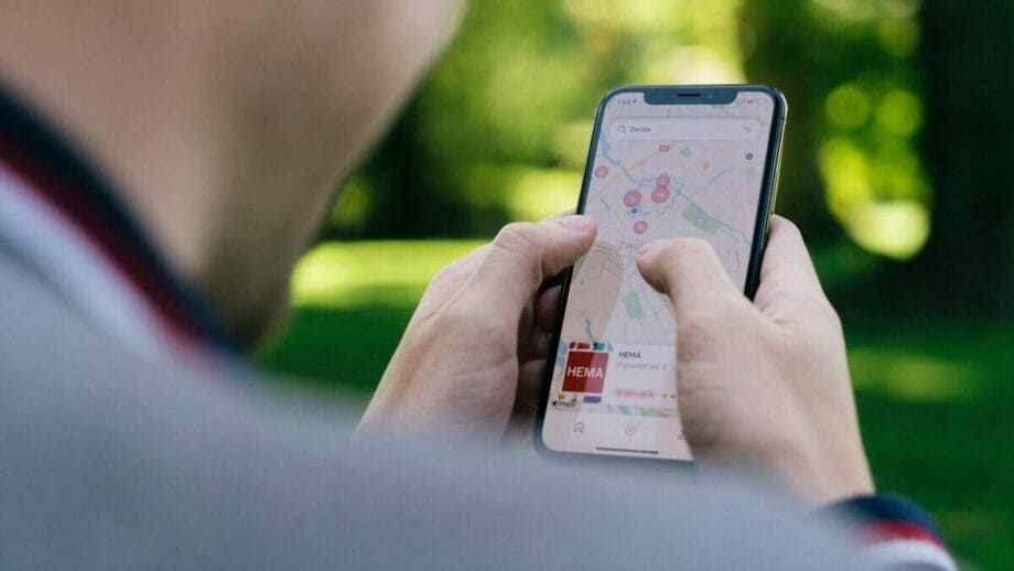 Person using a smartphone to navigate with a map app outdoors in a park setting.