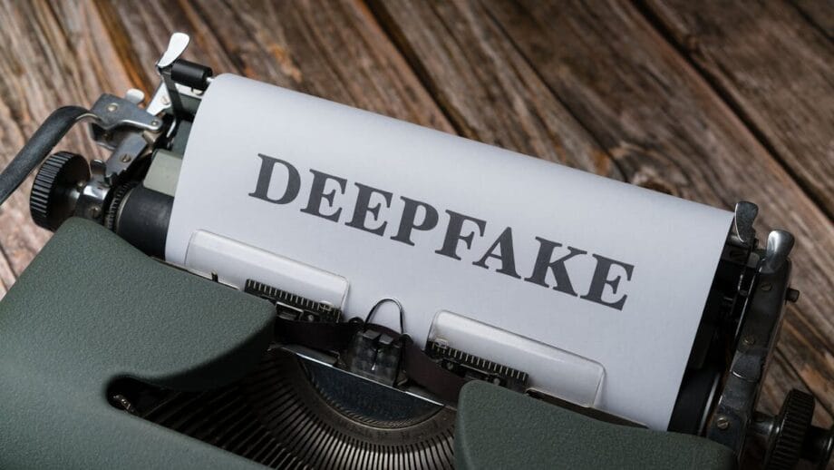 A typewriter with a sheet of paper displaying the word DEEPFAKE in bold, set on a wooden surface.