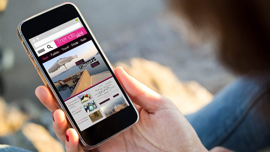 Person holding a smartphone displaying a website with categories like fashion, travel, and lifestyle. The screen shows images and text blocks.
