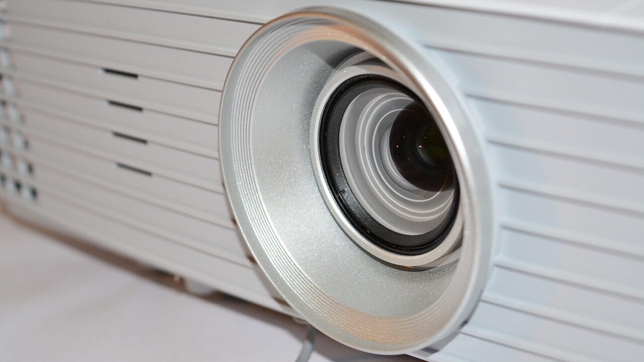 Close-up of a silver projector lens, showing the round casing and focus ring on a white background.