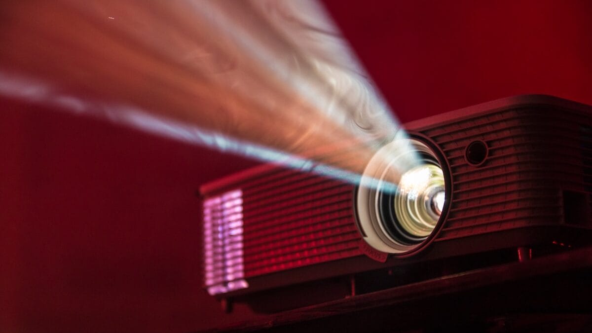 A projector emits a bright light beam against a red background.
