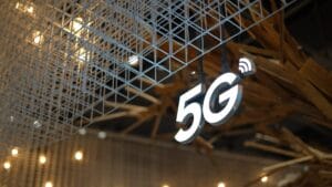 A glowing 5G sign hangs under a metal grid structure with small lights blurred in the background.