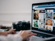 Person browsing a website with various images on a laptop at a desk, with a mug and camera in the background.