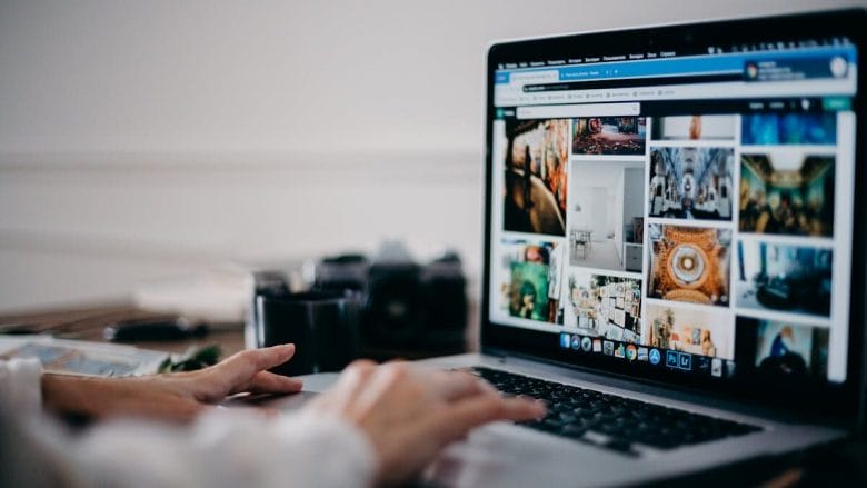 Person browsing a website with various images on a laptop at a desk, with a mug and camera in the background.