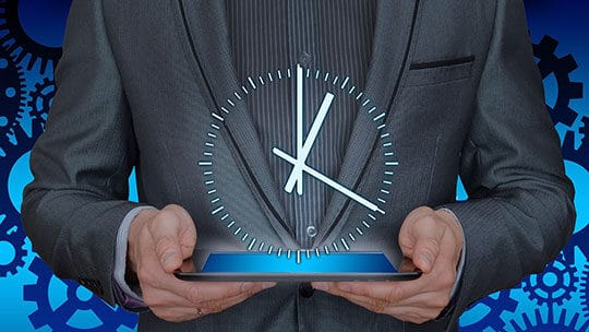 A man in a suit holds a tablet with a holographic clock displaying 9:00. Gears are visible in the background.