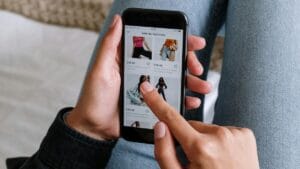 A person browses clothing items on a smartphone while sitting with legs crossed on a bed.