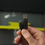A hand holding a braided cable with a USB-A connector and a USB-C connector in front of an open box.