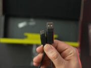 A hand holding a braided cable with a USB-A connector and a USB-C connector in front of an open box.