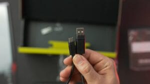 A hand holding a braided cable with a USB-A connector and a USB-C connector in front of an open box.