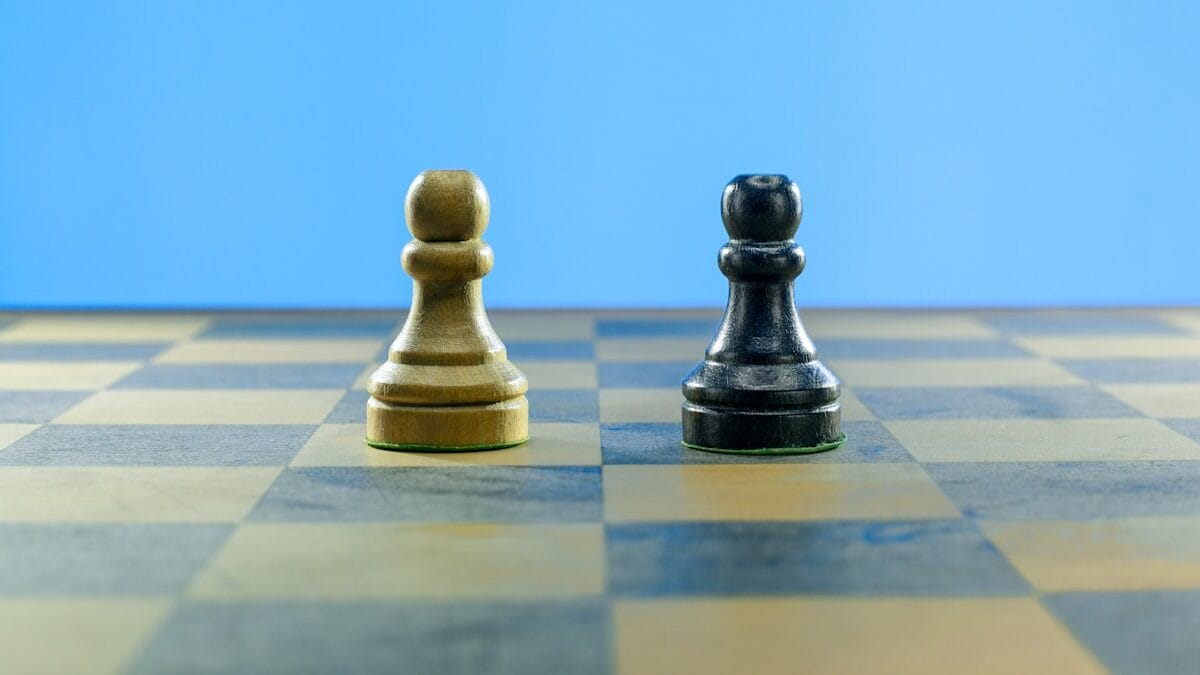 Two chess pawns, one light and one dark, stand side by side on a chessboard with a blue background.