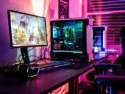 A gaming setup with a desktop PC, monitor, keyboard, mouse, headphones, and LED lighting in a room with blinds.