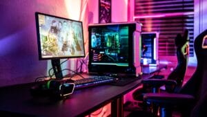 A gaming setup with a desktop PC, monitor, keyboard, mouse, headphones, and LED lighting in a room with blinds.