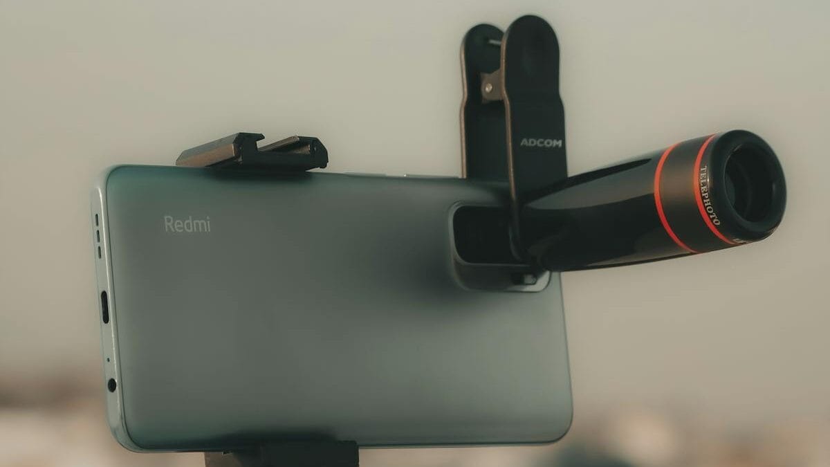 A smartphone mounted on a flexible tripod with a detachable zoom lens attached to the camera.
