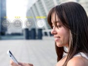 Woman outdoors looking at her phone, with a row of five emoticon rating icons and star ratings superimposed in front of her.