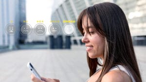 Woman outdoors looking at her phone, with a row of five emoticon rating icons and star ratings superimposed in front of her.