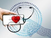A human hand and a digital hand interact with a smartphone displaying a heart and stethoscope, surrounded by binary code.