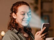 A woman uses facial recognition on her smartphone while holding a mug and smiling.