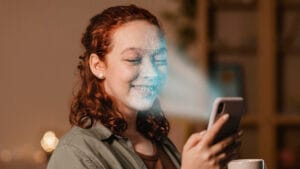 A woman uses facial recognition on her smartphone while holding a mug and smiling.