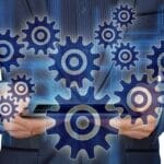 Person in a suit holding a tablet with digital gears and cogs overlayed, representing technology and process automation.