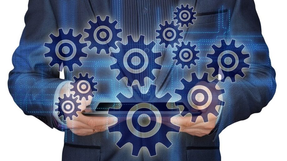 Person in a suit holding a tablet with digital gears and cogs overlayed, representing technology and process automation.