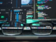 A pair of eyeglasses rests on a laptop keyboard with programming code displayed on the laptop screen in the background.
