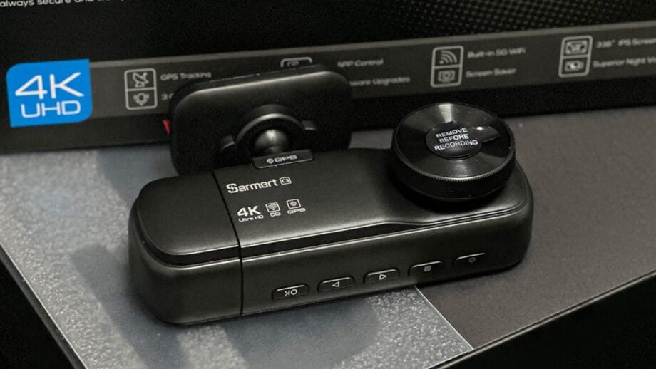 Sarmert C3 4K 3 Channel Dash Cam with GPS sits on a table, featuring several buttons and a lens cover that reads Remove before recording.
