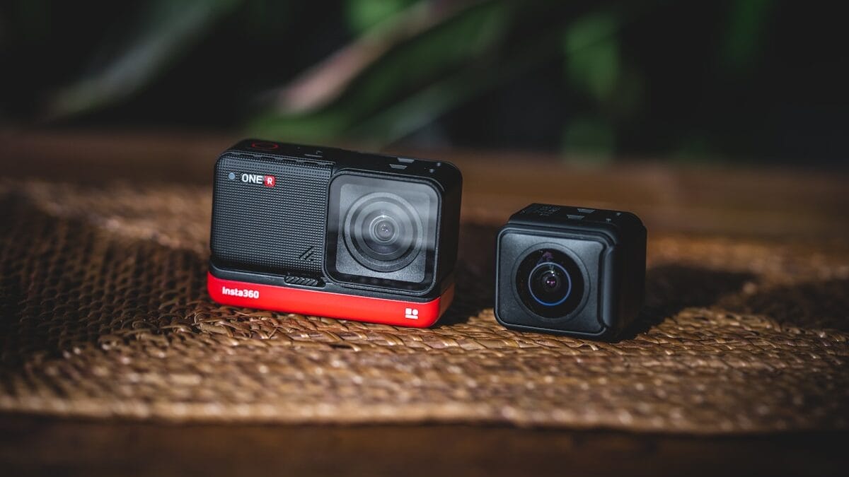 Two compact action cameras are placed side by side on a woven surface, with a blurred background.