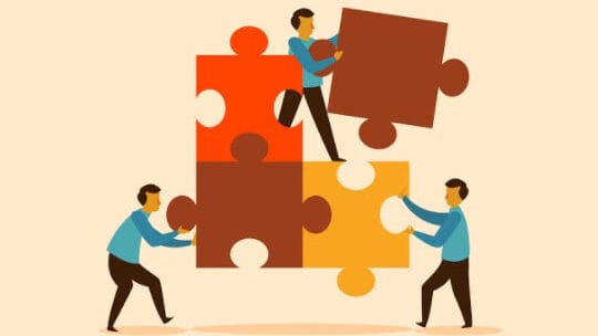 Three people in blue shirts assemble large puzzle pieces in red, brown, and yellow tones, symbolizing teamwork and collaboration.