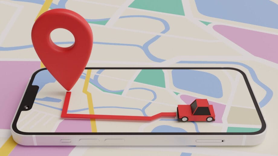 A smartphone displays a digital map with a red route, location pin, and a small red car on top of the screen.